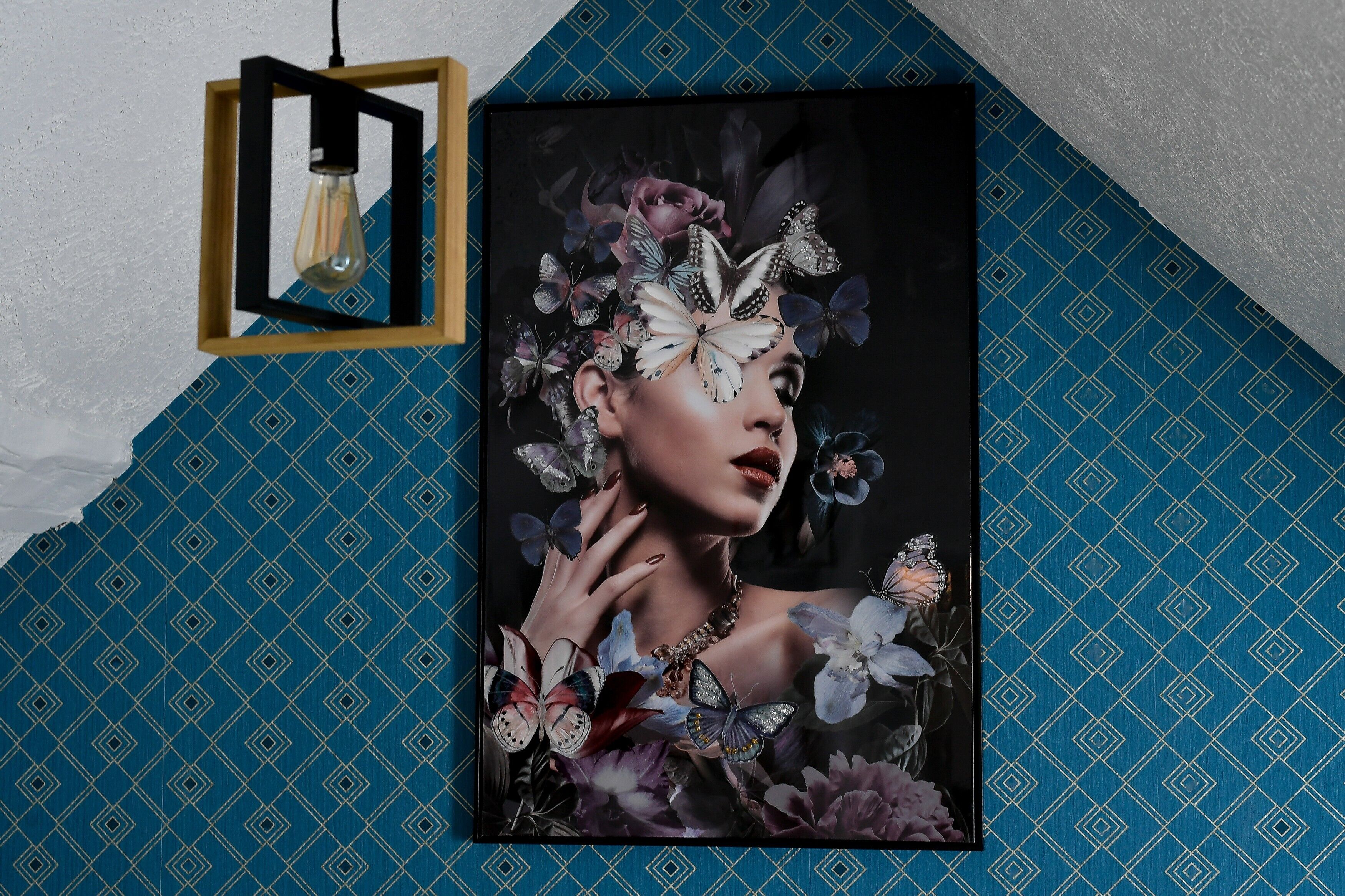 Een lijst met een kunstwerk met bloemen en vlinders, bevestigd aan een muur met behang met een geometrisch patroon.