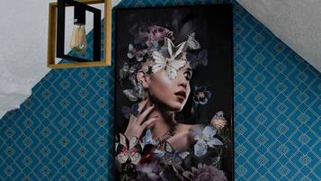 Een lijst met een kunstwerk met bloemen en vlinders, bevestigd aan een muur met behang met een geometrisch patroon.
