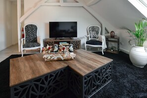 Una sala de estar tipo loft acogedora, con una mesa de centro de madera, dos sillones estampados, un televisor de pantalla plana y una planta grande en maceta.