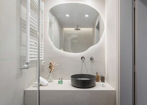 A modern bathroom with a curved mirror, a round sink, and a shower. - Glyfada Prime Living (Glyfada)