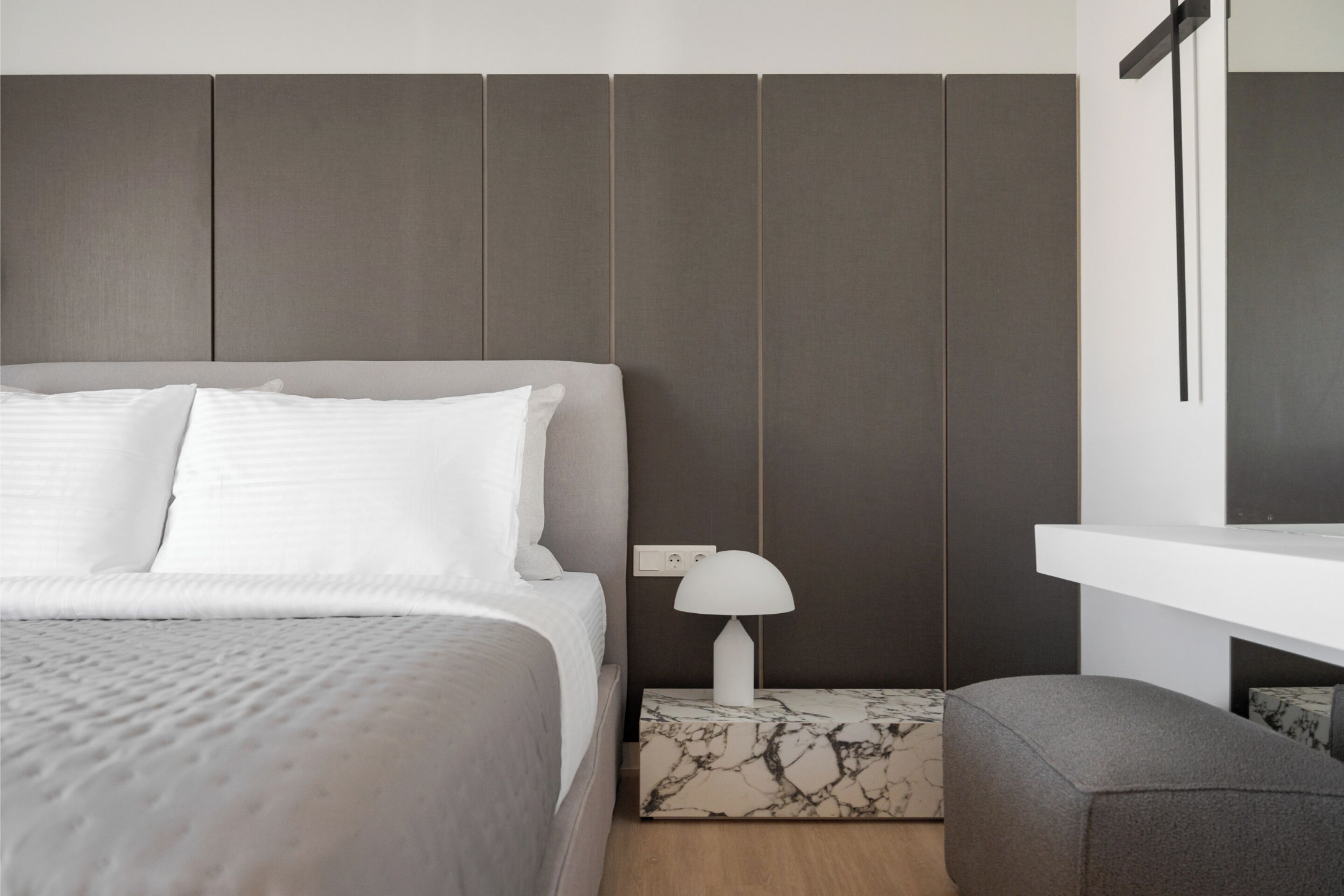 A modern bedroom with a bed, a nightstand, a lamp, and a small seating area.