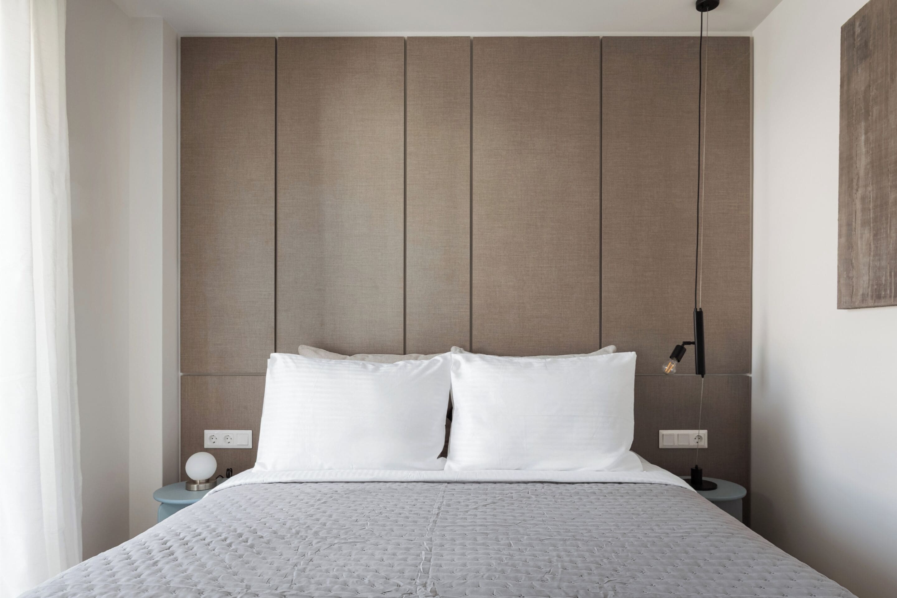 A modern hotel room with a large bed, a wooden headboard, and a bedside table with a lamp.
