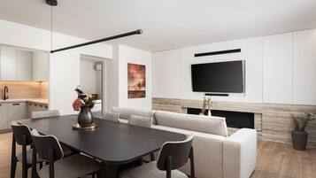 Un salon moderne comprenant un canapé, une table à manger avec des chaises, un téléviseur à écran plat fixé au mur et une cheminée.