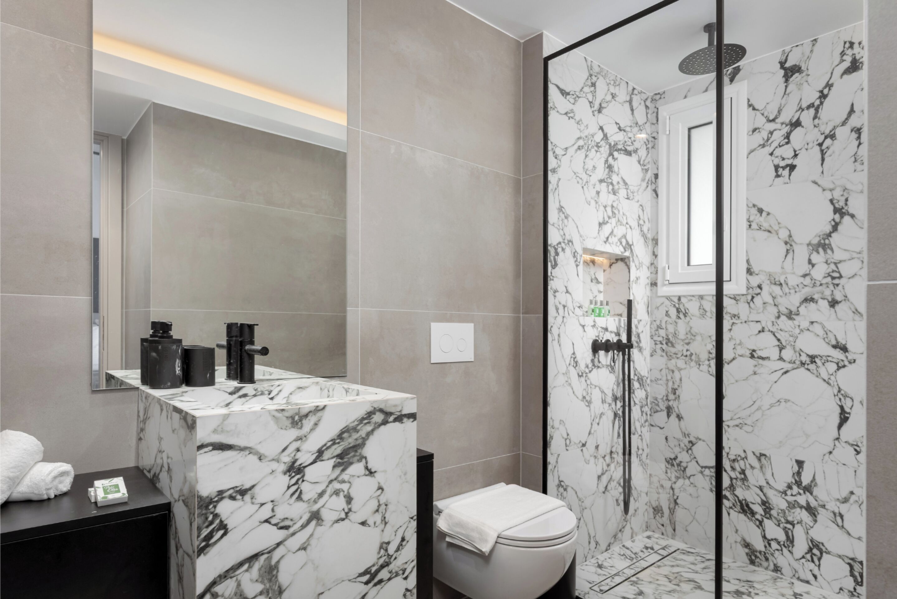 Un baño moderno con lavamanos de mármol, inodoro y ducha con puerta de cristal.
