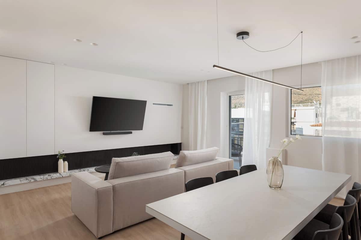A modern living room with a flat-screen TV, a sofa, a dining table, and a vase with flowers.