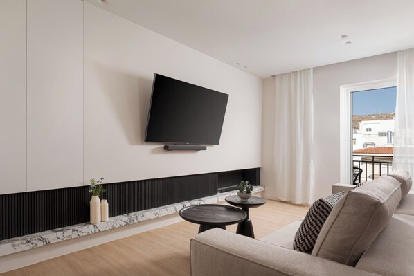 A modern living room with a flat-screen TV mounted on the wall, a sofa, a small round table, and a plant on a marble shelf. - Glyfada Prime Living (Glyfada)