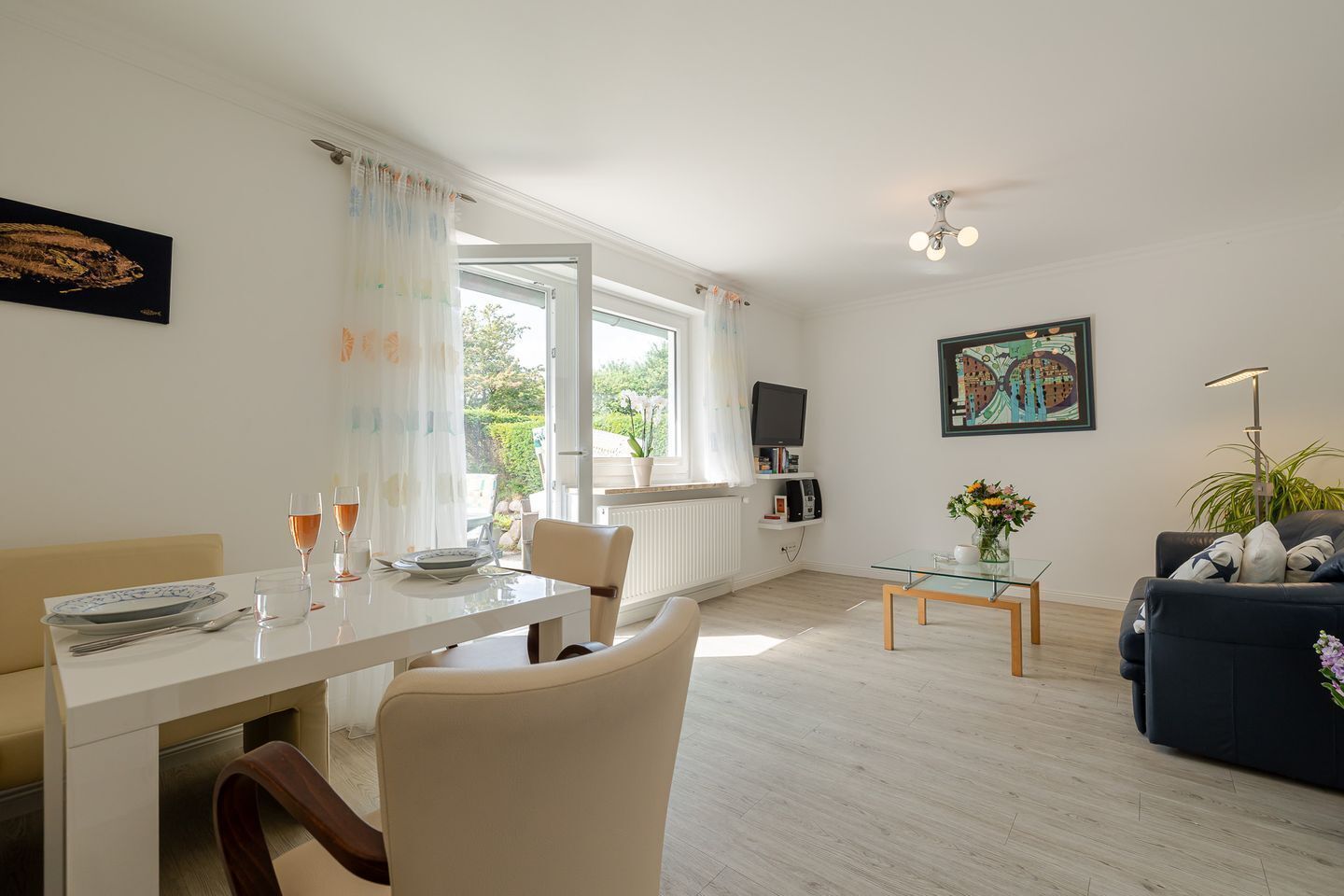En moderne stue med spiseplads, en sofa, et fjernsyn og kunst på væggene.