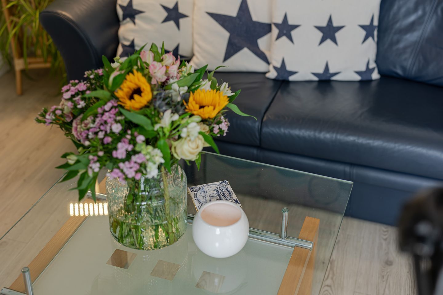 Et sofabord af glas med en vase med blomster og et hvidt lys.