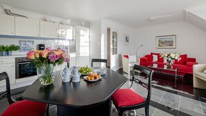 A modern kitchen with white cabinets, a dining table with red chairs, and a red sofa in the living area. - Strand - Lust auf Sylt - Apartment Strand for 2 persons (Sylt-Ost)