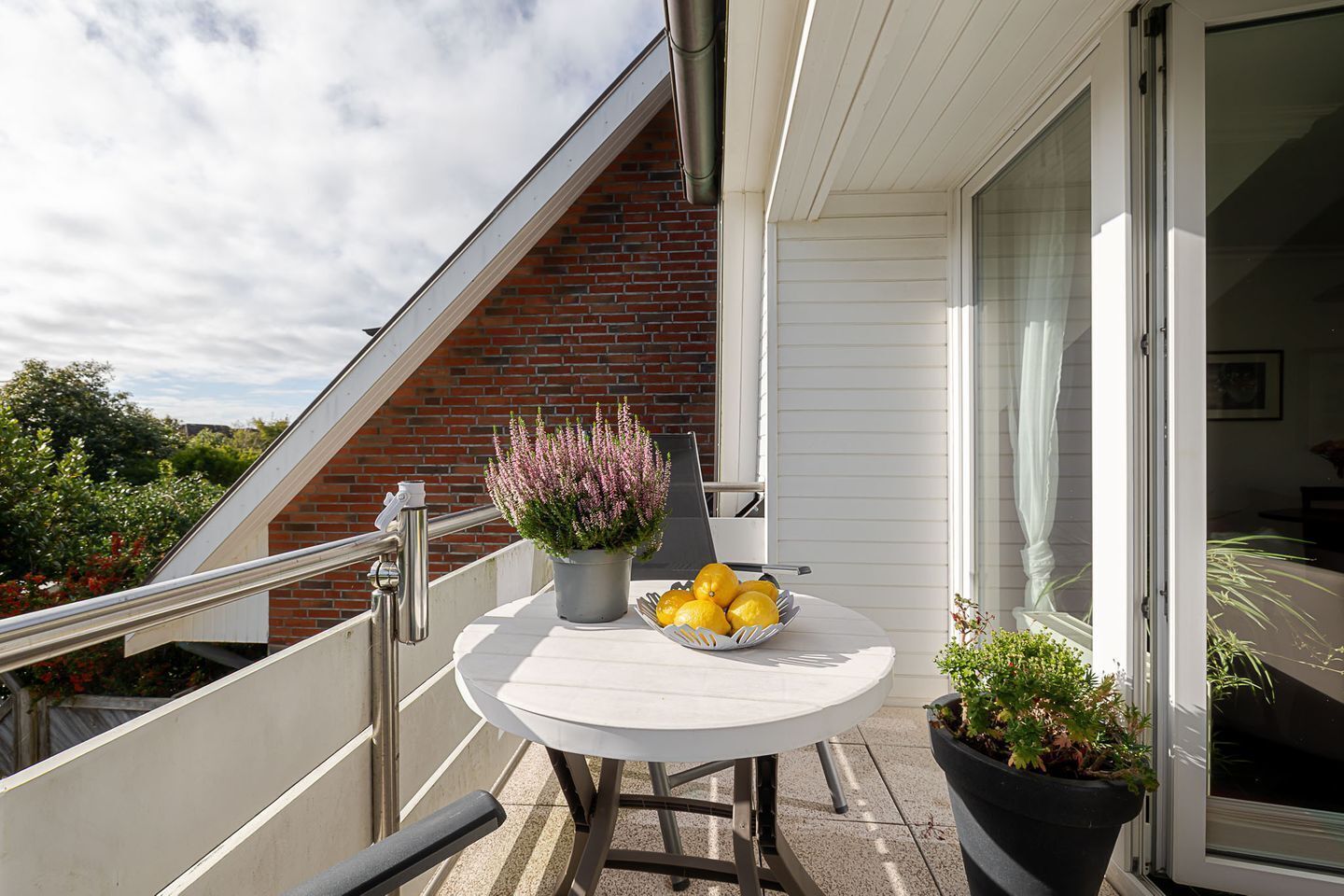 A balcony with a round table, potted plants, and a bowl of lemons.