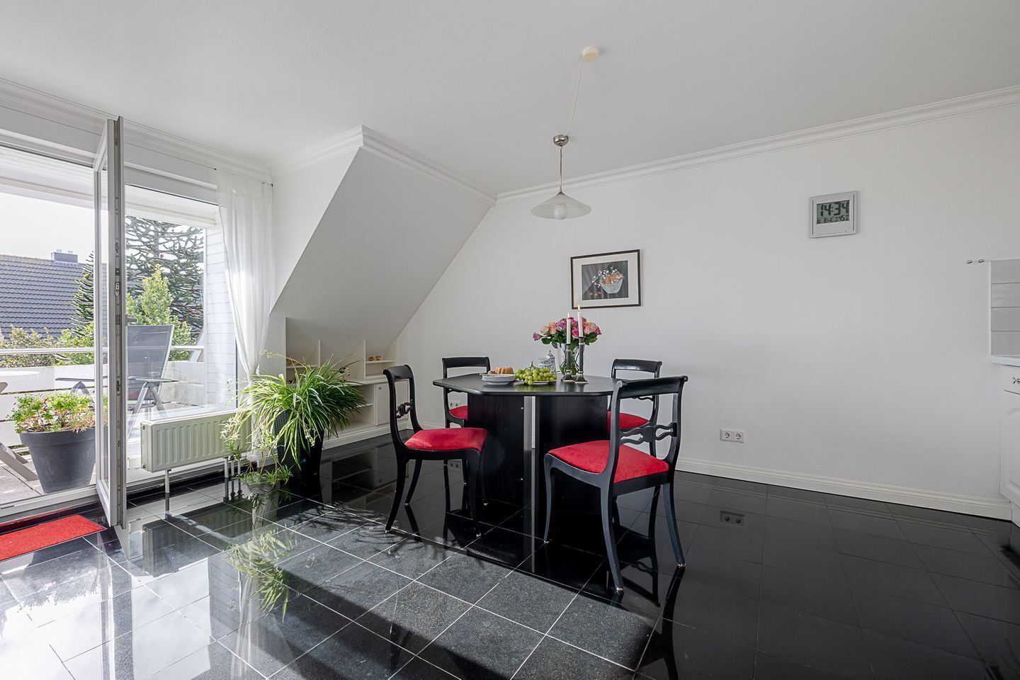 A dining area with a black table and chairs, a potted plant, and a window with a view of the outside.