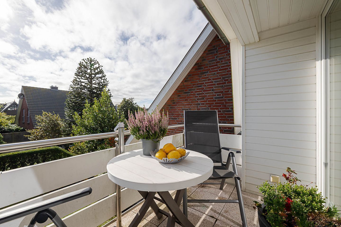 Un balcon avec une table ronde, une chaise, un pot de fleurs et un saladier de fruits.