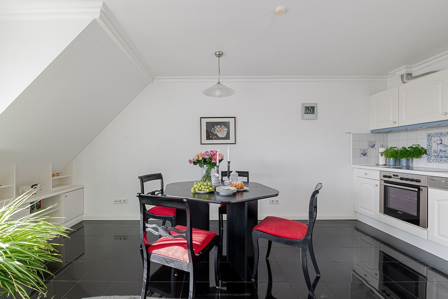 A modern kitchen with white cabinetry, a dining table with red chairs, and a clock on the wall.