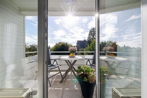 A balcony with a table and chairs, a potted plant, and a view of the sky and buildings.