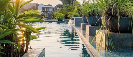 En swimmingpool med klart vand, omgivet af beplantning og en flisekant.