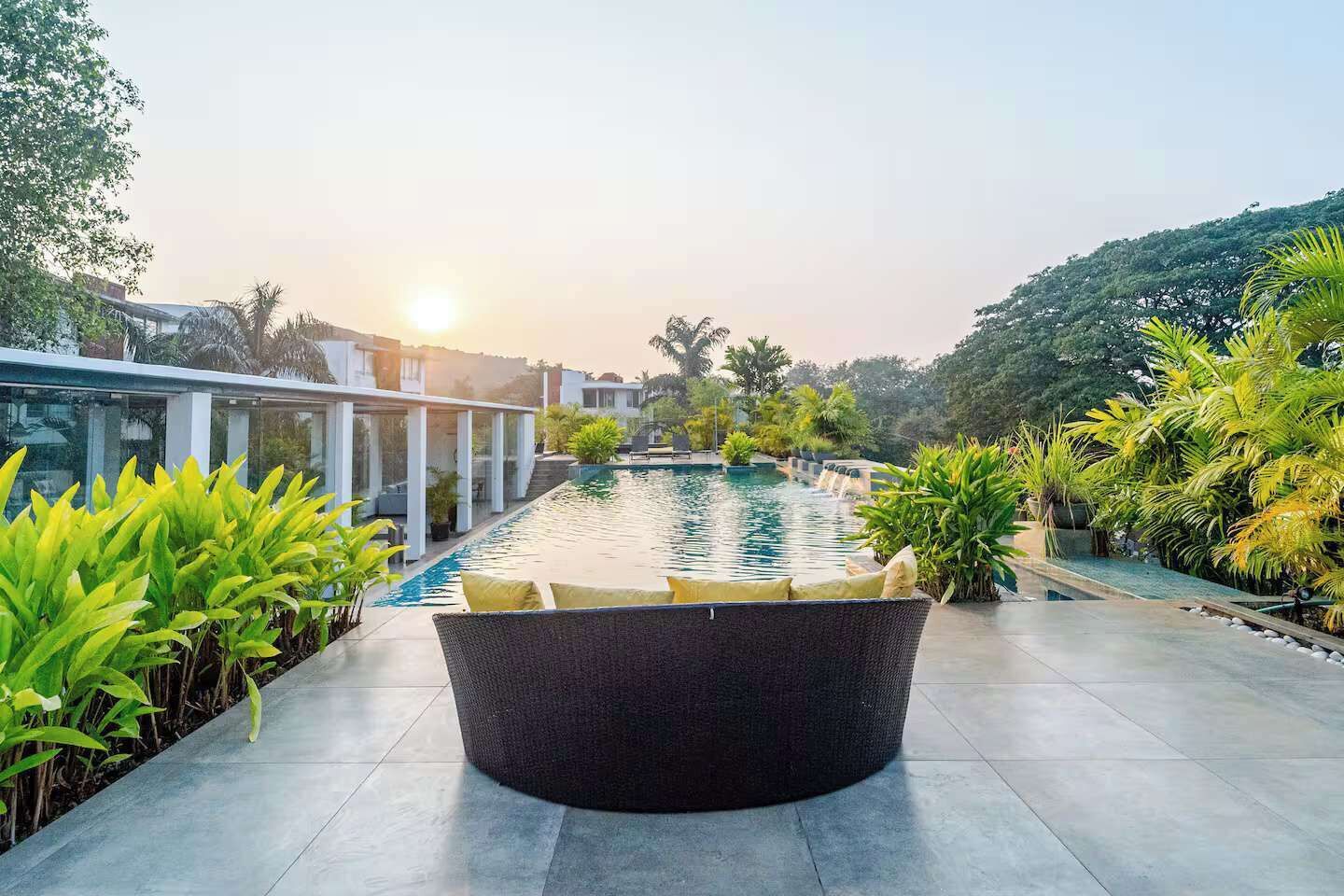 A modern outdoor pool area with a circular seating area, surrounded by lush greenery and a clear sky.