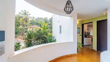 Una habitación con un balcón curvo, una cocina al fondo y vistas a palmeras y casas.