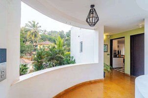 Una habitación con un balcón curvo, una cocina al fondo y vistas a palmeras y casas.