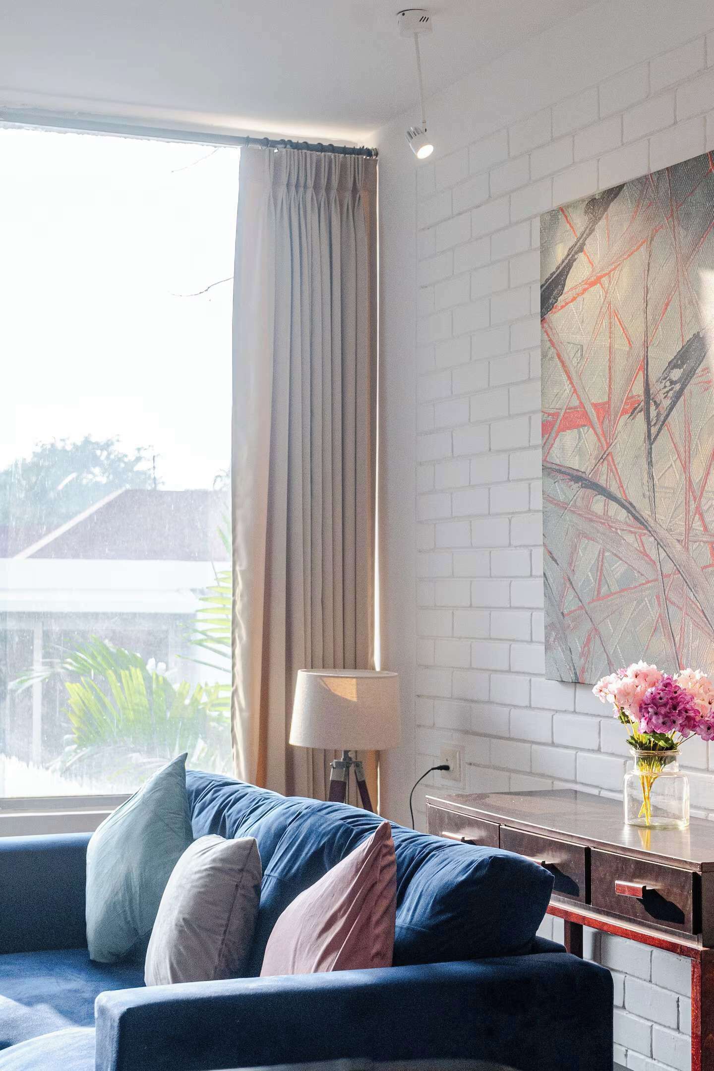 A modern living room with a blue sofa, a vase of flowers, and a large abstract painting on the wall.