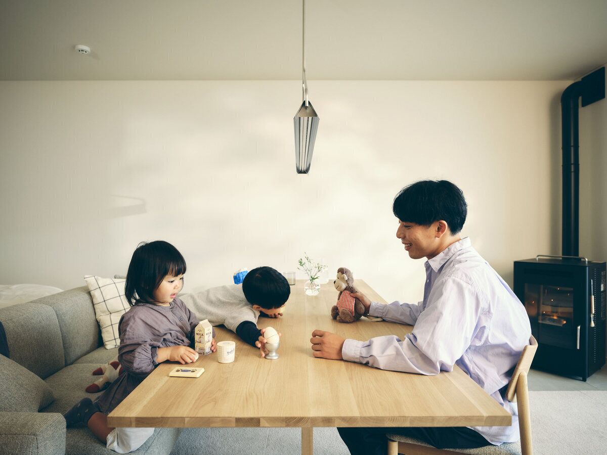 Una famiglia di tre persone a un tavolo da pranzo in legno in un soggiorno moderno con un divano, una piccola pianta e un camino.