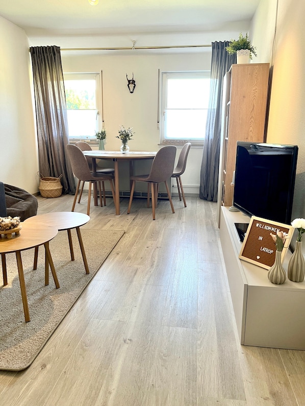 A modern living room with a dining area, a flat-screen TV, and a welcome sign.