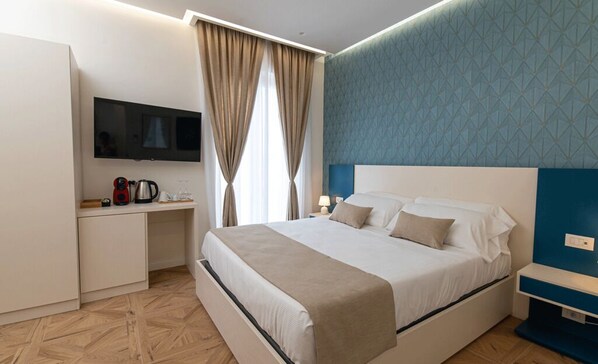 A hotel room with a bed, a TV mounted on the wall, a desk with a kettle, and a window with curtains. - Don Salvatore (Monte di Procida)