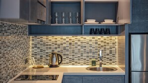 A modern kitchen with a tiled backsplash, a stainless steel sink, and a built-in cabinet with glassware and plates. - Rooftop Pool Gym 600 m to Beach C161 (Kamala)