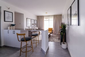 A modern kitchen with a central island, bar stools, and a dining area with a yellow chair.