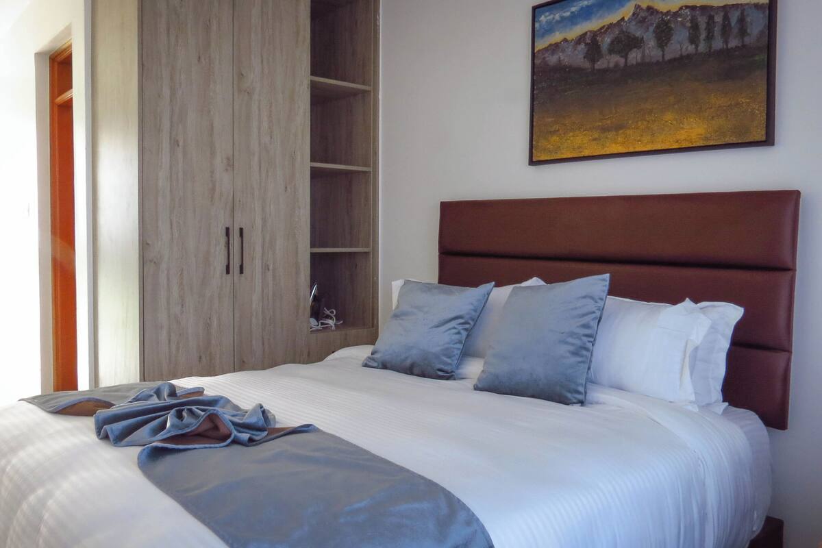 A bedroom with a bed, a wooden wardrobe, and a painting on the wall.