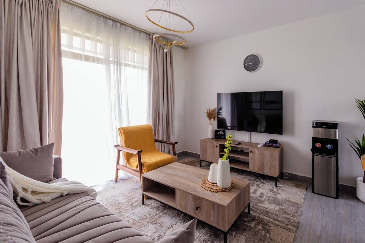 A modern living room with a sofa, armchair, coffee table, TV, and a water dispenser.
