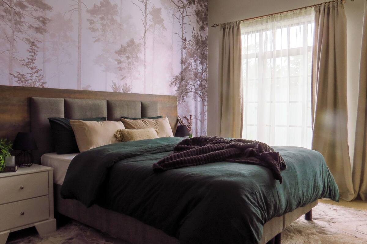 A bedroom with a bed, nightstand, and a large window with curtains.