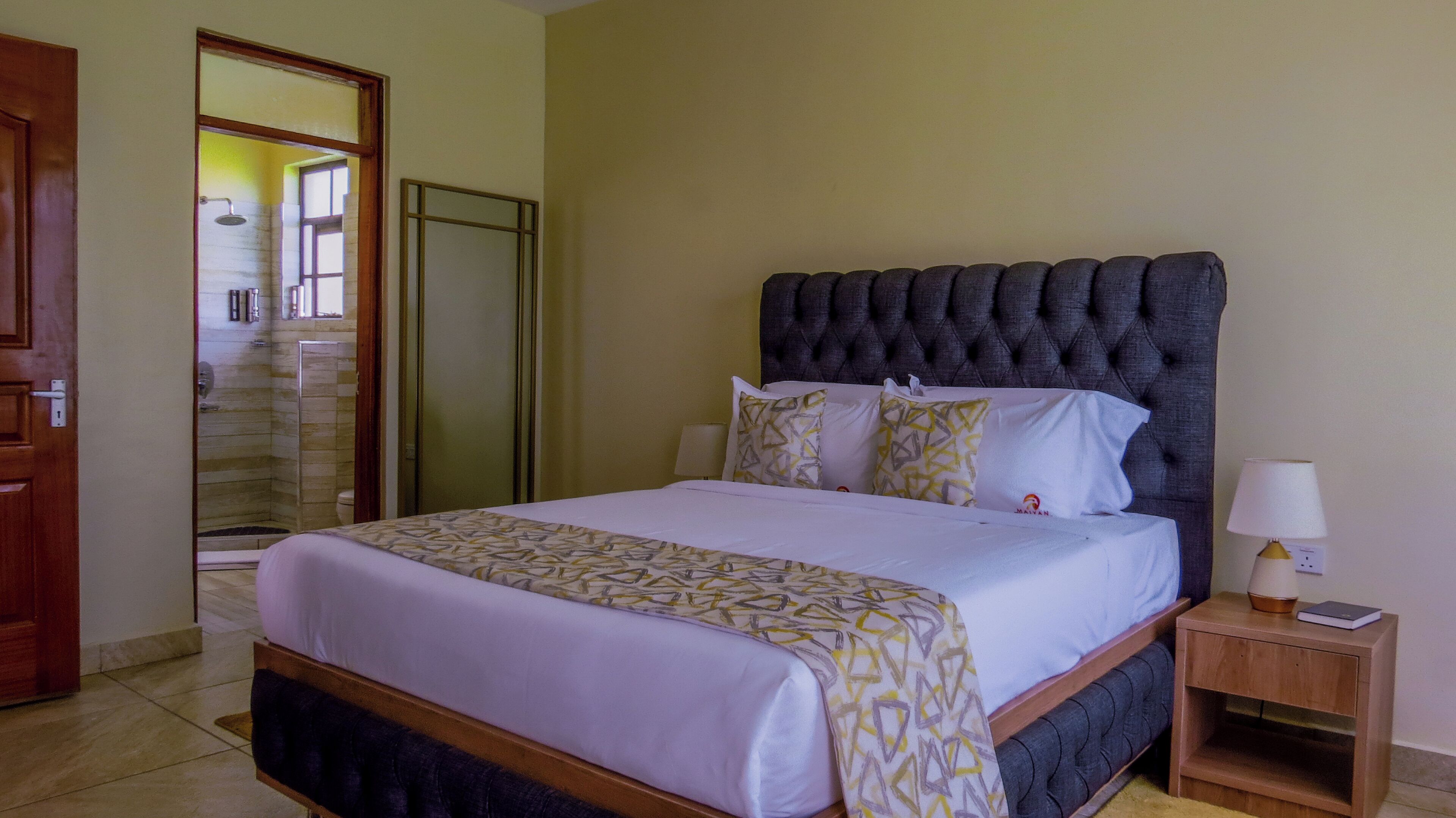 A hotel room with a large bed, a bedside table with a lamp, and a bathroom visible through an open door.