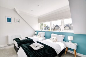 A modern bedroom with two beds, a window with a view of buildings, and a white radiator. - The Loft at The Regency (Harrogate)
