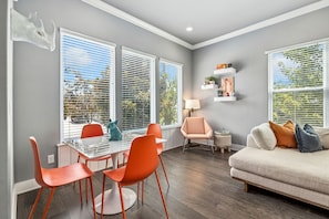 A modern living room with a dining area, large windows with blinds, a sofa, and a small table with chairs. - Passage - Arts District - Garage - 0.5 mi DT (Bentonville)