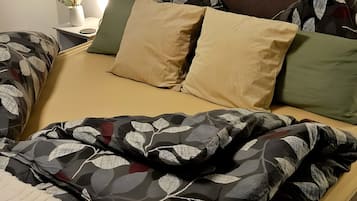 Ein Bett mit gemusterten Betttextilien, ein Nachttisch mit einer Pflanze und Wandkunst.