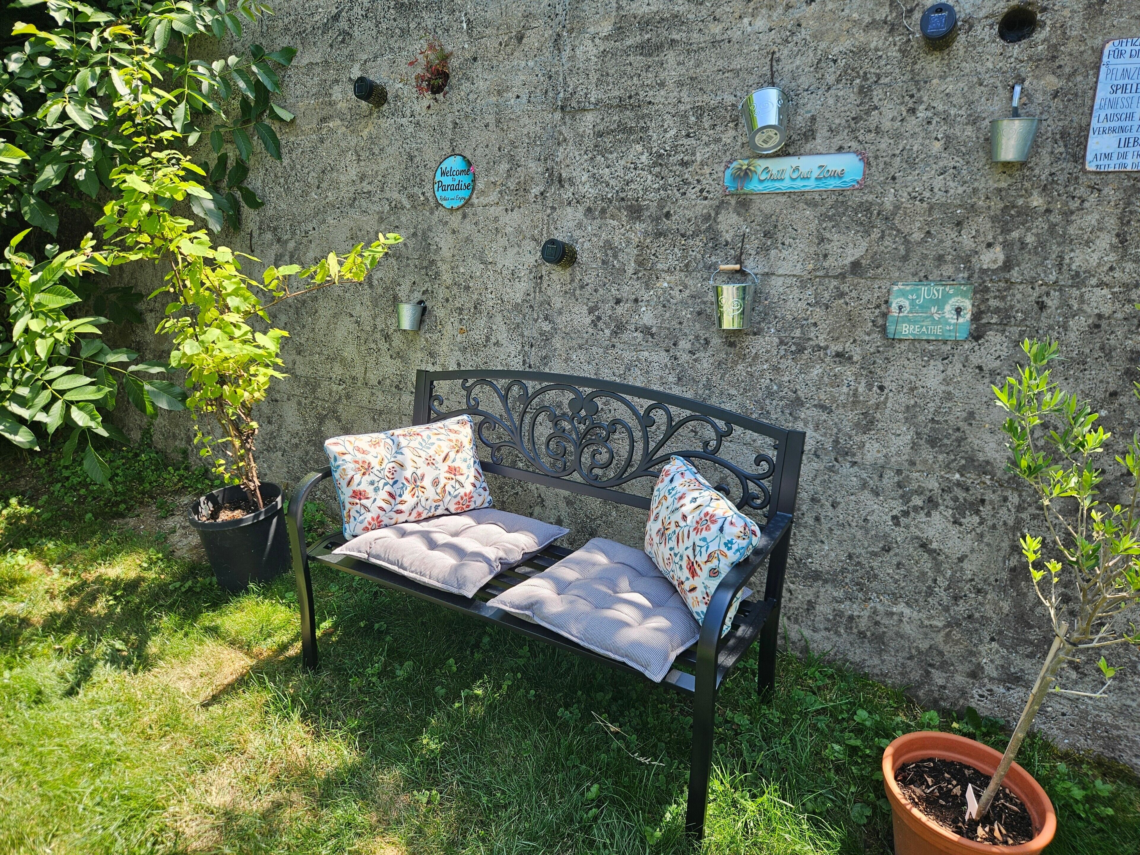 Un banc agrémenté de coussins à motifs floraux, une plante en pot et un mur orné de différents panneaux.