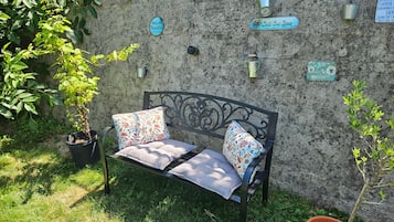 Un banc agrémenté de coussins à motifs floraux, une plante en pot et un mur orné de différents panneaux.