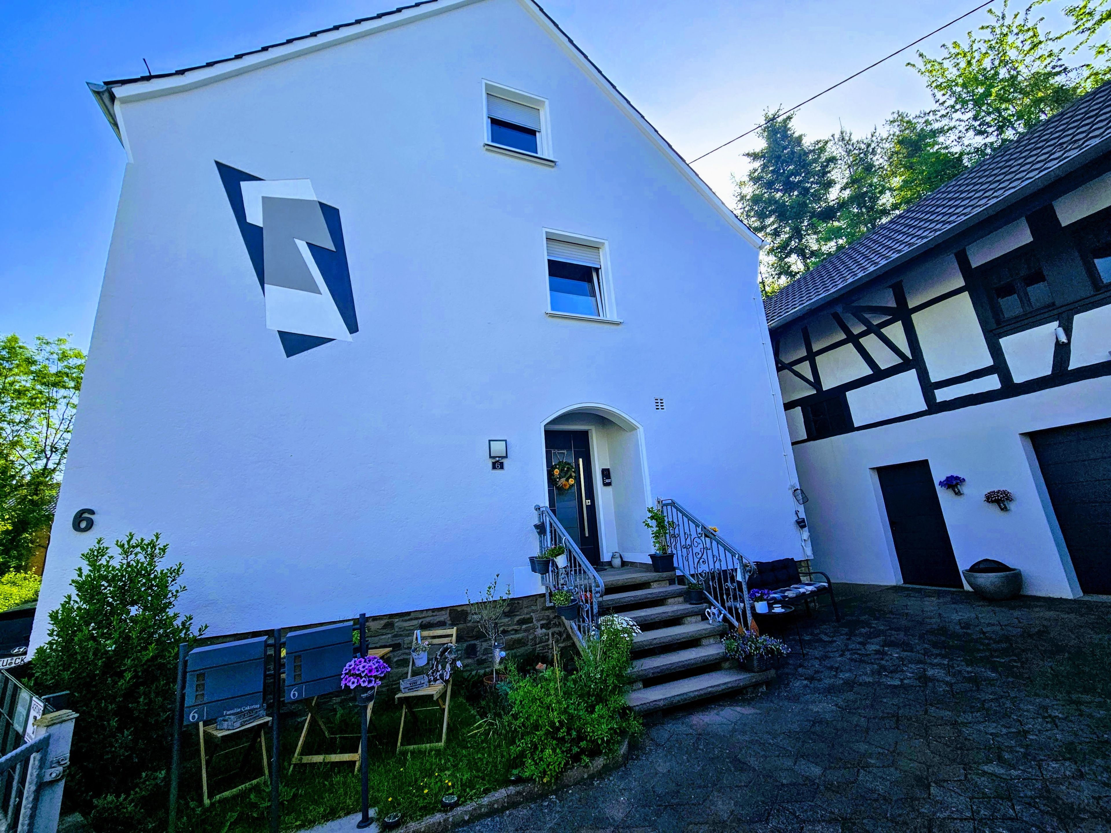 Ein zweistöckiges Gebäude mit einem großen, geometrischen Logo an der Fassade, einem Eingang mit einer Tür und einer Treppe, die zu der zweiten Etage führt.