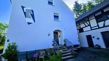Ein zweistöckiges Gebäude mit einem großen, geometrischen Logo an der Fassade, einem Eingang mit einer Tür und einer Treppe, die zu der zweiten Etage führt.