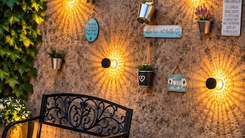 Een bank voor een met textuur beklede muur, voorzien van meerdere wandlampen en plantenpotten.
