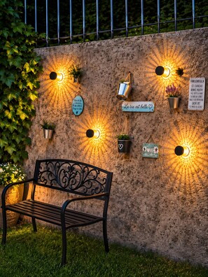 A bench in front of a textured wall with multiple wall-mounted lights and potted plants. - Elya Apartment – Garden Paradise near Events, Outlet, and Spa (Bad Münstereifel)