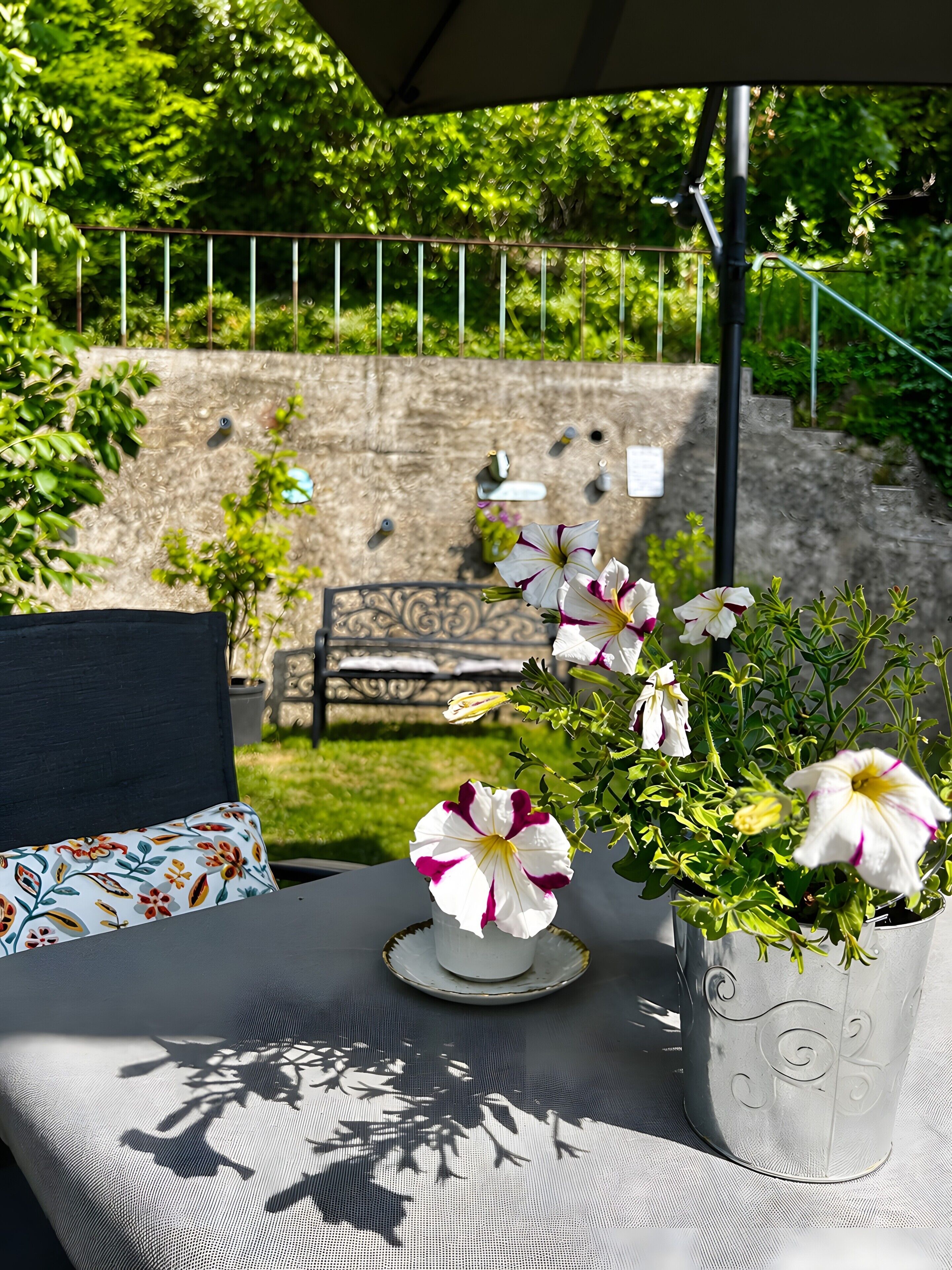 En patio med et bord, en potteplante med blomster og en stenvæg i baggrunden.
