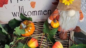Un panneau décoratif représentant un gnome et des feuilles d’automne, placé à côté d’un panier en osier rempli de citrouilles et de feuillages.