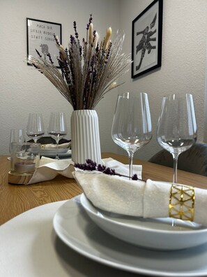 A dining table set with white plates, clear wine glasses, and a vase with dried flowers. - Elya Apartment – Garden Paradise near Events, Outlet, and Spa (Bad Münstereifel)