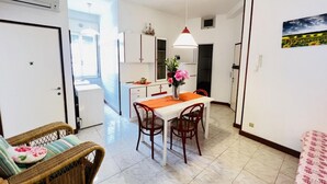 A compact kitchen with white cabinets, a dining table with two chairs, and a hanging pendant light. - Spacious Flat in the Centre of Bibione (San Michele al Tagliamento)