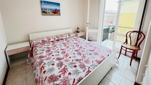 A bedroom with a bed, a nightstand, a chair, a balcony, and a hanging light fixture. - Spacious Flat in the Centre of Bibione (San Michele al Tagliamento)