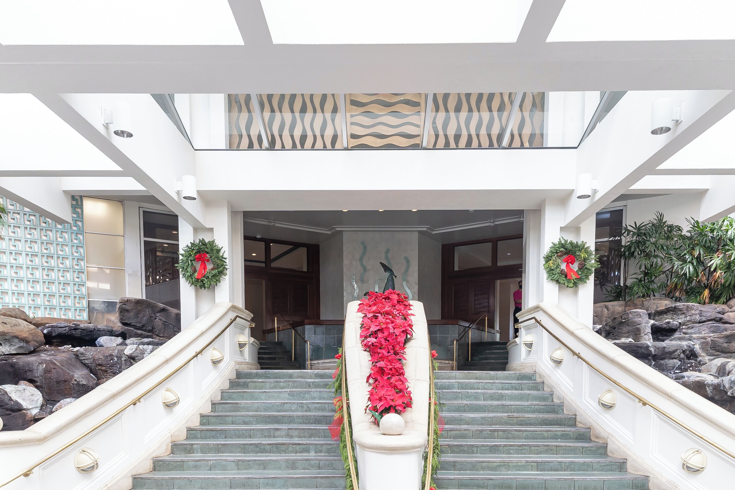 Una majestuosa escalera con un arreglo floral en la parte superior, que conduce a un vestíbulo de techos altos y diseño moderno.