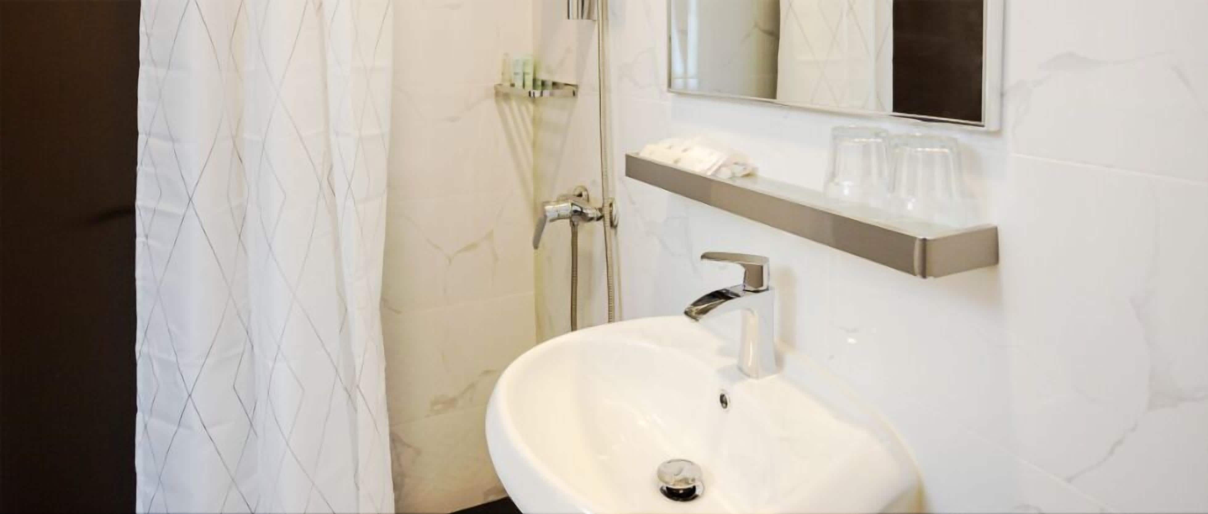 Un baño con un lavamanos blanco, un espejo y una repisa con vasos y artículos de aseo.