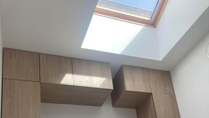 A bedroom with a skylight, built-in wooden cabinets, a bed with white bedding, and a white headboard. - T2 30 M² 4 Sleeps max close to shops and 4-way access (Guignen)
