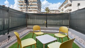 Une terrasse avec des chaises jaunes et une table, entourée d’une pelouse verdoyante et d’une clôture.